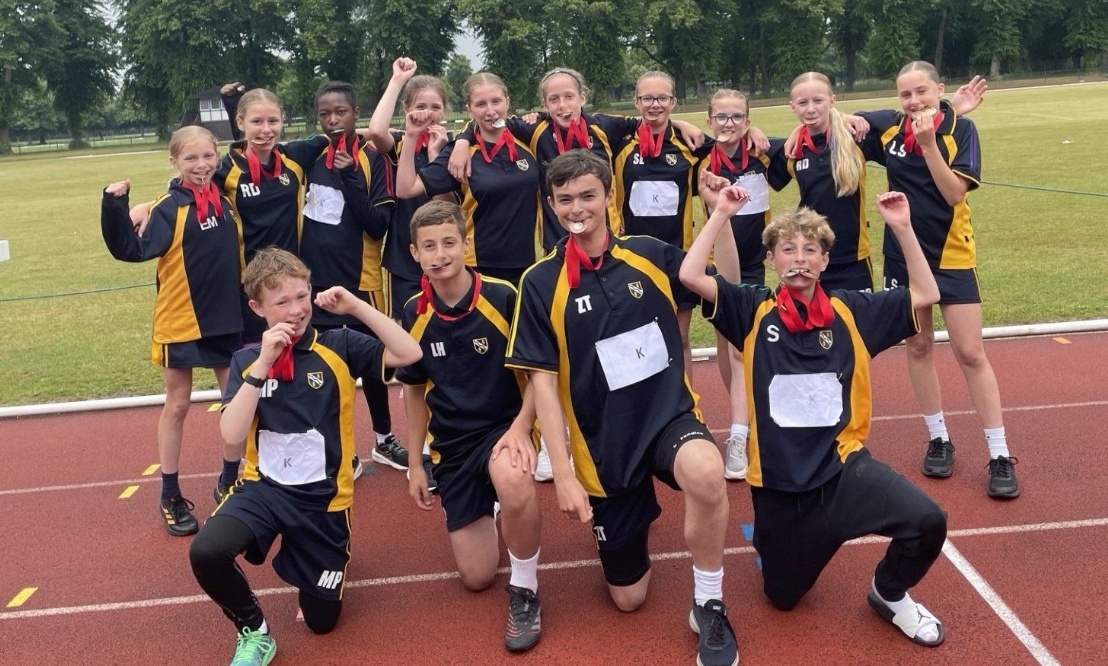Kennet Year 7 pupils celebrating their District Sports Day success by holding their medals in their teeth and smiling for the camera.